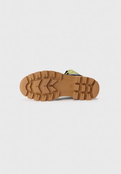 Mångfärgad sandal sula med ett texturerat gummigrepp mönster, featuring djupa spår och en tan färg, designad för grepp och stabilitet.