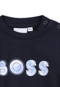 Sweatshirt bleu marine avec un col rond, des boutons aux épaules et un graphique "BOSS" audacieux en bleu clair.