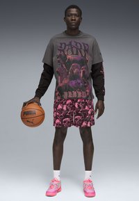 Szary i czarny t-shirt graficzny z oversize'owym krojem; różowe szorty w czaszki; różowo-szare sneakersy; trzymający piłkę do koszykówki.