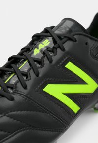 Melnas futbola kurpes ar teksturētu ādu, ar spilgti zaļu "N" logotipu, numurētu "442" detaļu un melnu šņoru.