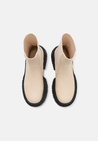 Beige leather ankle boots with a rounded toe, black textured rubber sole, and elastic side panels for easy wear.