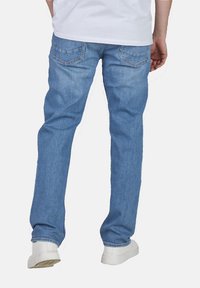 Vaqueros de mezclilla azul deslavado con corte recto, que cuentan con dos bolsillos traseros y detalles de costura sutiles, combinados con zapatillas blancas.