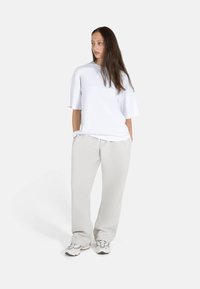 Hvit oversized t-skjorte med korte ermer, kombinert med lysegrå løstsittende bukser og beige sneakers. Enkel, glatt stoff og uformelt design.