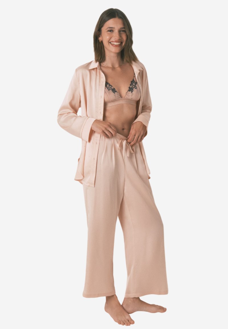 Pyjamasset i mjuk rosa siden. Inkluderar en skjorta med krage och långa ärmar samt löst sittande byxor med snörning i midjan.