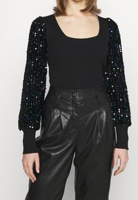 Body noir côtelé avec manches longues bouffantes ornées de sequins. Pantalon en cuir noir taille haute avec plis à l'avant et fermeture par bouton.
