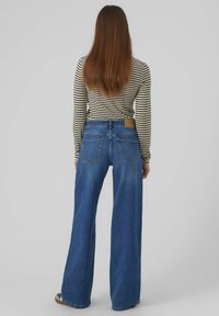Weite blaue Jeans aus Denim, mit hoher Taille, fünf Taschen-Design und einer hellen Waschung. Kombiniert mit einem gestreiften Langarmoberteil.