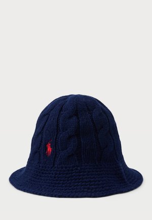 Cappello a secchiello lavorato a maglia di colore navy, con texture a trecce, ampia visiera e un piccolo logo ricamato in rosso sul lato. Materiale in morbida lana.