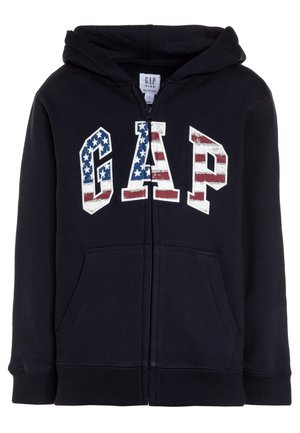 Navyblå hættejakke med lynlås, der har en forlommekængurulomme og et grafisk "GAP"-logo med et amerikansk flagdesign i rødt, hvidt og blåt.