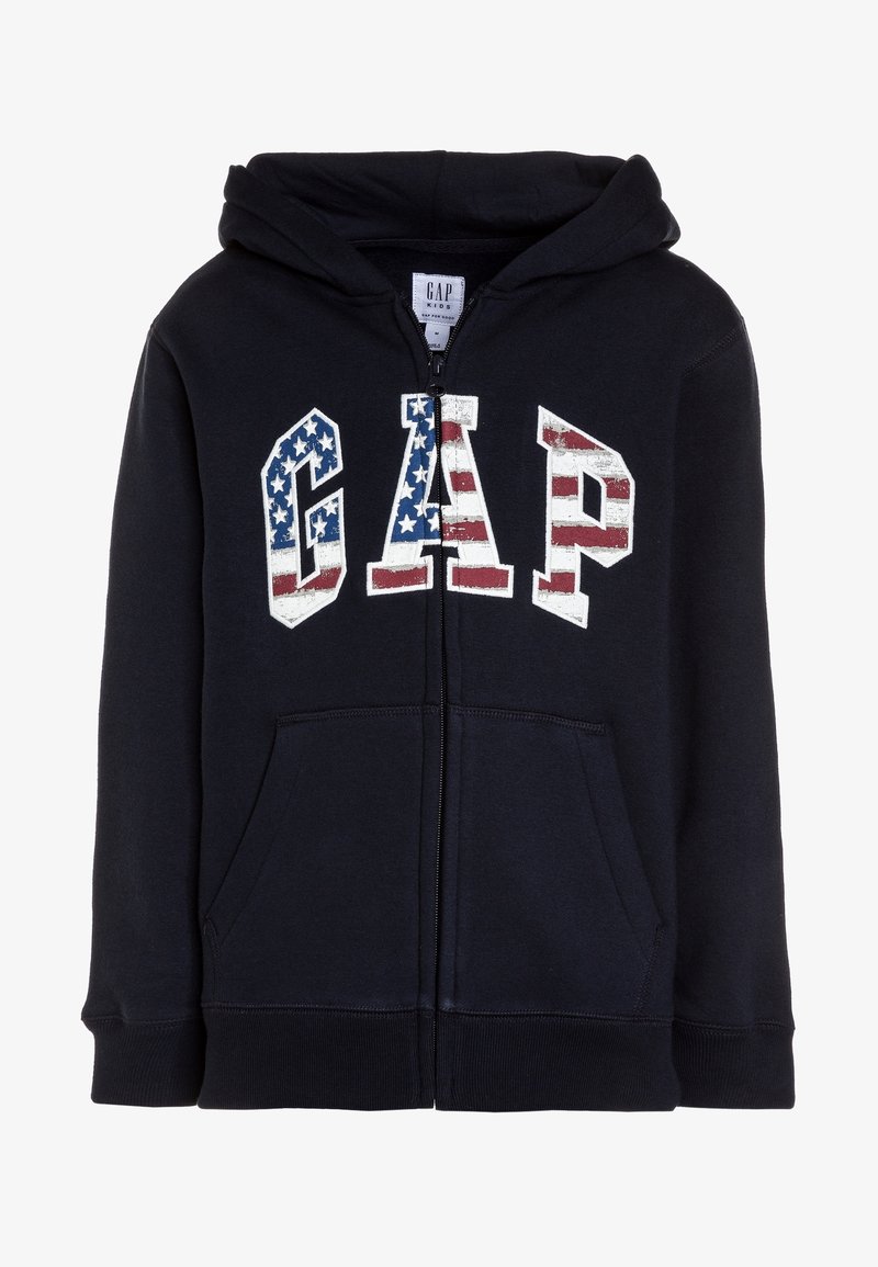 Sweat à capuche zippé en tissu bleu marine, doté d'une poche kangourou à l'avant et d'un logo graphique "GAP" avec un motif de drapeau américain en rouge, blanc et bleu.