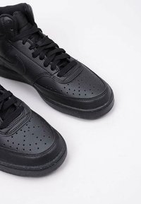 Sneaker alte in pelle nera con puntale perforato, lacci neri piatti, tomaia testurizzata e suola in gomma con un discreto design maculato.