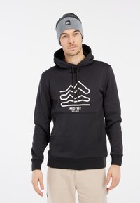 Zwarte sweatshirt met capuchon, voorzien van een witte grafische print aan de voorkant en een kangoeroezak. Gecombineerd met een grijze beanie.