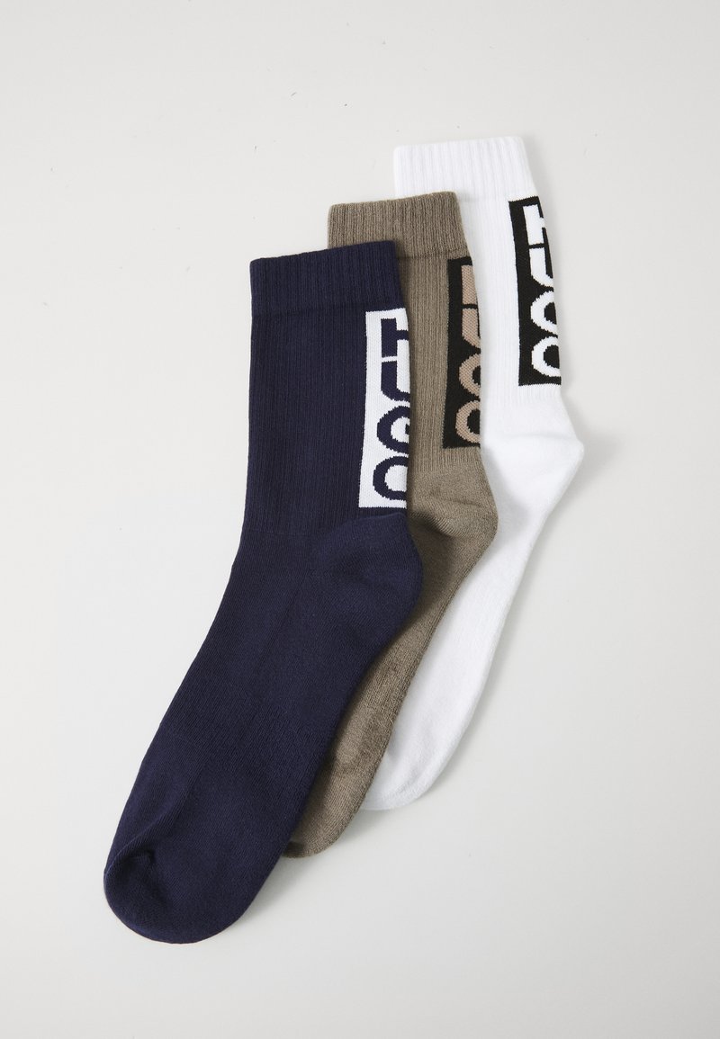 Trois paires de chaussettes de sport : bleu marine, vert olive et blanc. Chacune a une finition texturée avec un logo imprimé sur le côté.