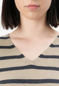 Beige v-halsgenser med svarte horisontale striper. Myk tekstur og strikket materiale. Ingen synlige logoer eller utsmykninger.