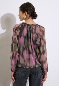 Gennemsigtig bluse med et multikolor mønster i pink, grøn og brun; lange ærmer, rynket halsudskæring og elastiske manchetter. Sammen med mørke jeans.