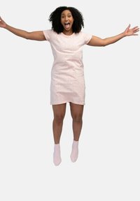 Abito rosa chiaro con piccole macchie colorate; maniche corte; lunghezza al ginocchio; abbinato a calzini alla caviglia rosa chiaro; modella che salta, braccia distese.