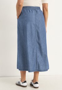 Jeanskjol med avslappnad passform, elastisk midja, längd till mitten av vaden och sidofickor. Bärs med vita och svarta sneakers.