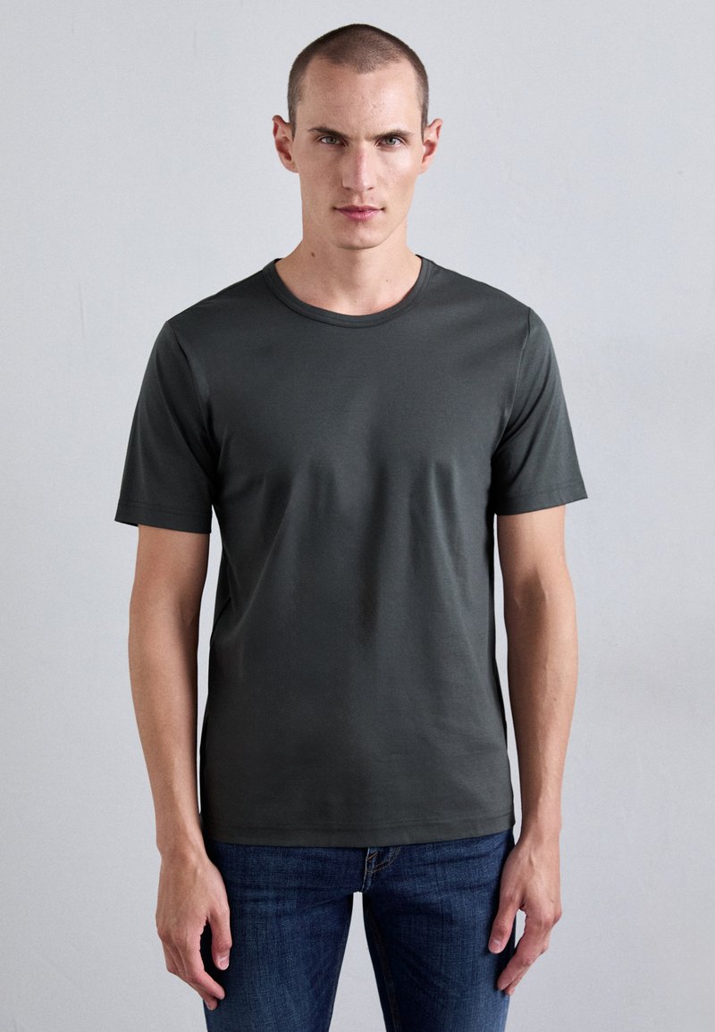 T-shirt court à manches courtes vert foncé, col rond, en mélange de coton lisse. Porté avec un jean bleu, design ajusté avec des coutures minimales.