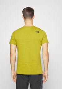 Olijfgroene T-shirt met korte mouwen van een zachte stof, met een ronde halslijn en het logo van The North Face in het zwart gedrukt op de bovenrug.