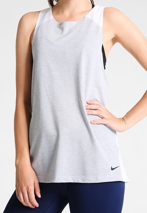 Kobieta ubrana w jasno szary bezrękawnik sportowy z małym czarnym logo Nike w dolnej prawej części, w połączeniu z ciemnoniebieskimi legginsami.