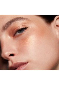Close-up of a face featuring smooth skin with a warm, bronzed complexion, lightly defined contours, and natural eyelashes.