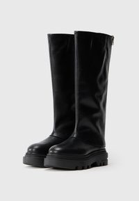 Botas negras hasta la rodilla, hechas de cuero suave, con una suela gruesa negra y un zipper lateral para facilitar su uso.