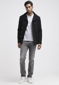 Fekete peacoat, dupla gombos záródással, világosszürke V-nyakú póló fölött viselve. Szürke farmernadrág és fehér sportcipő egészíti ki az outfitet.