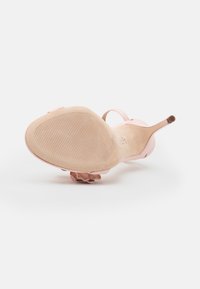 Różowa sandał na wysokim obcasie z teksturowaną gumową podeszwą. Posiada delikatny pasek oraz kwiatowy akcent przy pięcie. Gładki materiał.