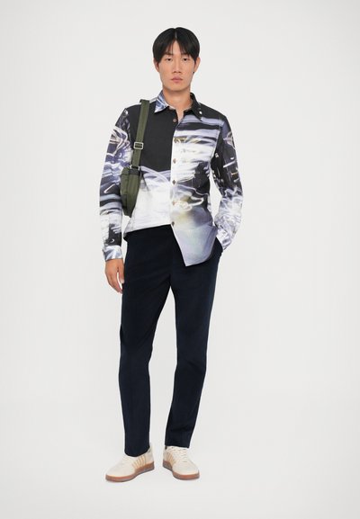 Zwart en veelkleurig overhemd met een grafisch dessin, gecombineerd met marineblauwe broeken en beige sneakers met bruine accenten.