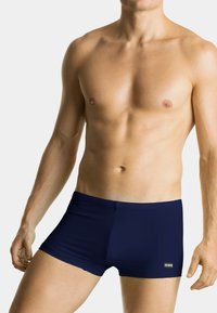 Granatowe kąpielówki wykonane z elastycznego materiału, charakteryzujące się dopasowanym krojem i gładką fakturą. Etykieta marki widoczna po prawej stronie.