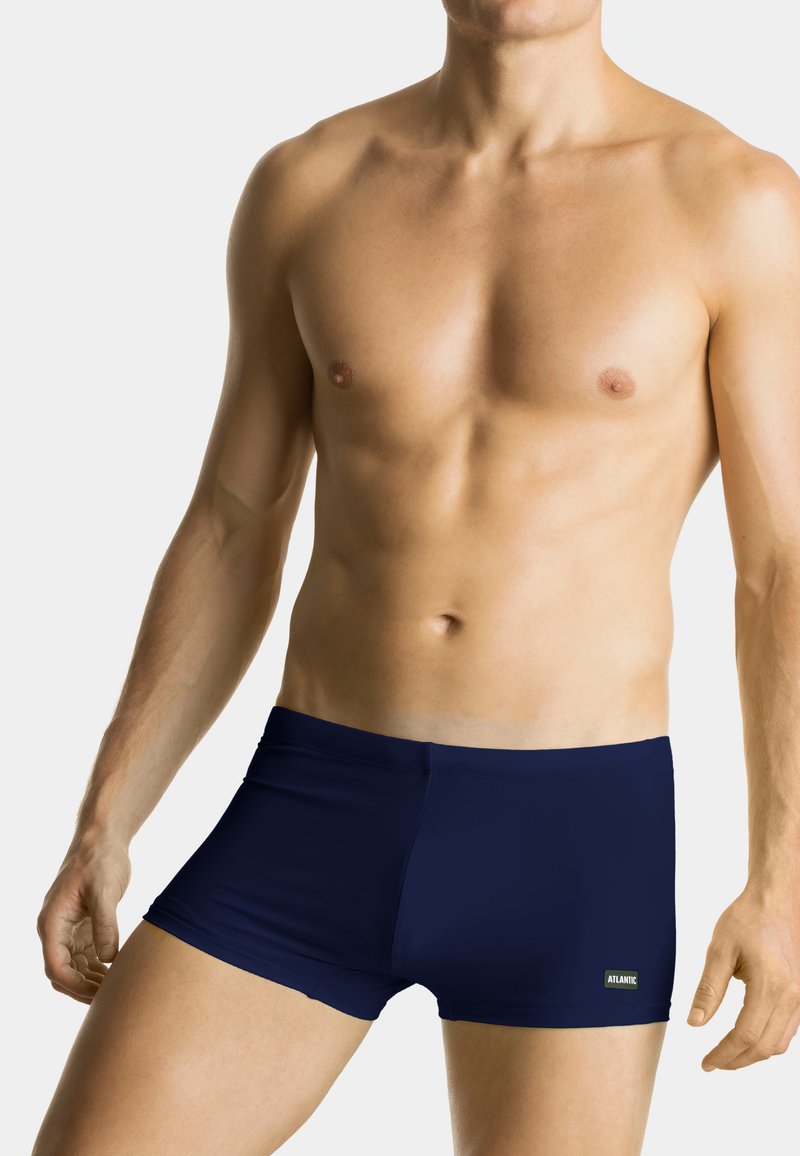 Granatowe kąpielówki wykonane z elastycznego materiału, charakteryzujące się dopasowanym krojem i gładką fakturą. Etykieta marki widoczna po prawej stronie.