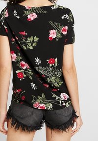 Camiseta negra con estampado floral, de manga corta y cuello redondo, combinada con pantalones cortos de mezclilla negra deshilachados. Patrones de flores en verde y rojo visibles.
