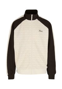 Jopica s visokim ovratnikom, zadrgo spredaj, v kremsko in temno rjavi barvni blokadi, z vzorčastim telesom in podrobnostmi logotipa. Ima elastične manšete in rob.