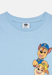 Lichtblauwe katoenen t-shirt met daarop twee cartoon honden met gedetailleerde gezichtsuitdrukkingen, die respectievelijk blauwe en gele hoeden dragen.