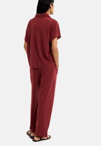 Bordowa koszulka polo z krótkim rękawem o luźnym kroju z detalem szwu z tyłu, zestawiona z pasującymi szerokimi spodniami. Lekką tkanina. Klapki.