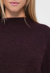 Burgundinsininen neulepusero, jossa on korkea kaulus; pehmeä, tekstuuriainen kangas; rento malli ja hienovaraiset värierot.
