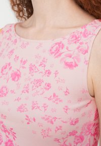 Κοντινό πλάνο ενός ατόμου που φοράει ροζ τοπ χωρίς μανίκια με σχέδιο φωτεινών ροζ λουλουδιών.