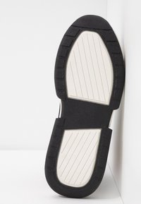 Černá gumová podrážka boty s texturovaným povrchem, bílá střední podrážka a výrazné drážky pro lep ší přilnavost. Úhlovitý tvar s zaoblenými okraji.