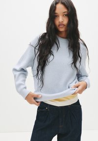 Maglione azzurro chiaro a coste con colletto a girocollo, abbinato a pantaloni in denim scuro. Il maglione presenta maniche lunghe e una vestibilità comoda.