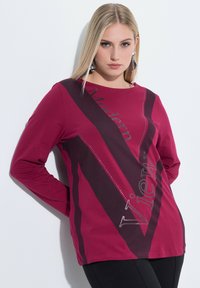 Langärmliges, weinrotes T-Shirt mit dunklen Akzenten und aufgedrucktem Text. Verfügt über einen Rundhalsausschnitt und eine glatte, weiche Textur.