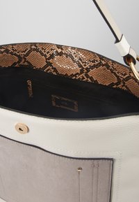 Vitt och beige handväska med guldknapp, ytterficka och inredning med ormskinnsmönster samt blixtlås-ficka.