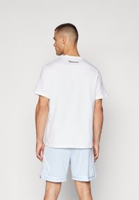 Hvit bomull T-skjorte med kort erme og Reebok-logo på øvre rygg. Kombinert med lyseblå mesh treningsshorts med side mønstre.