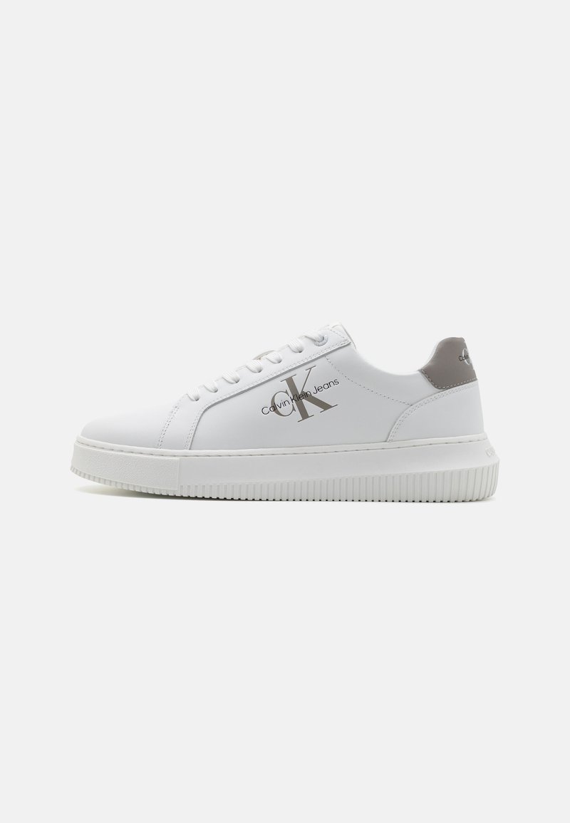 White synthetic sneaker with rounded toe, lace-up front, grey accent on heel, and branded logo in silver on the side. Textured rubber sole.