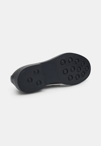 Suela de zapato con una superficie de goma negra lisa, que presenta patrones de tracción circulares y un talón redondeado para agarre y estabilidad.