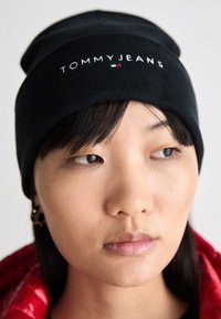 Czarna dzianinowa czapka z logo "TOMMYJEANS" w białym kolorze, z małym akcentem w trzech kolorach. Gładka tekstura i podwinięty krój.