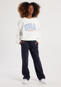 Felpa bianca con la scritta "USA" in azzurro chiaro e "New York City" in rosso. Abbinata a pantaloni della tuta blu navy e sneaker bianche.