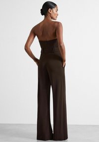Brun bärpumpslös jumpsuit med vida ben, åtsittande midja och sidofickor. Slätt material, minimalistic design och dold dragkedja bak.