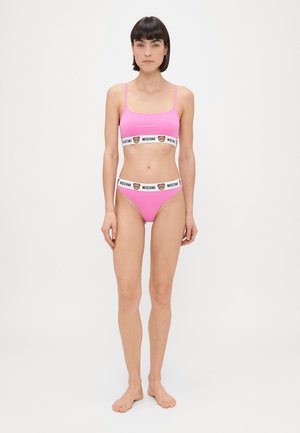 Lyserød to-delt sæt med en bralette med tynde stropper og bikini-bund, begge med en kontrasterende hvid bånd mærket "Moschino."