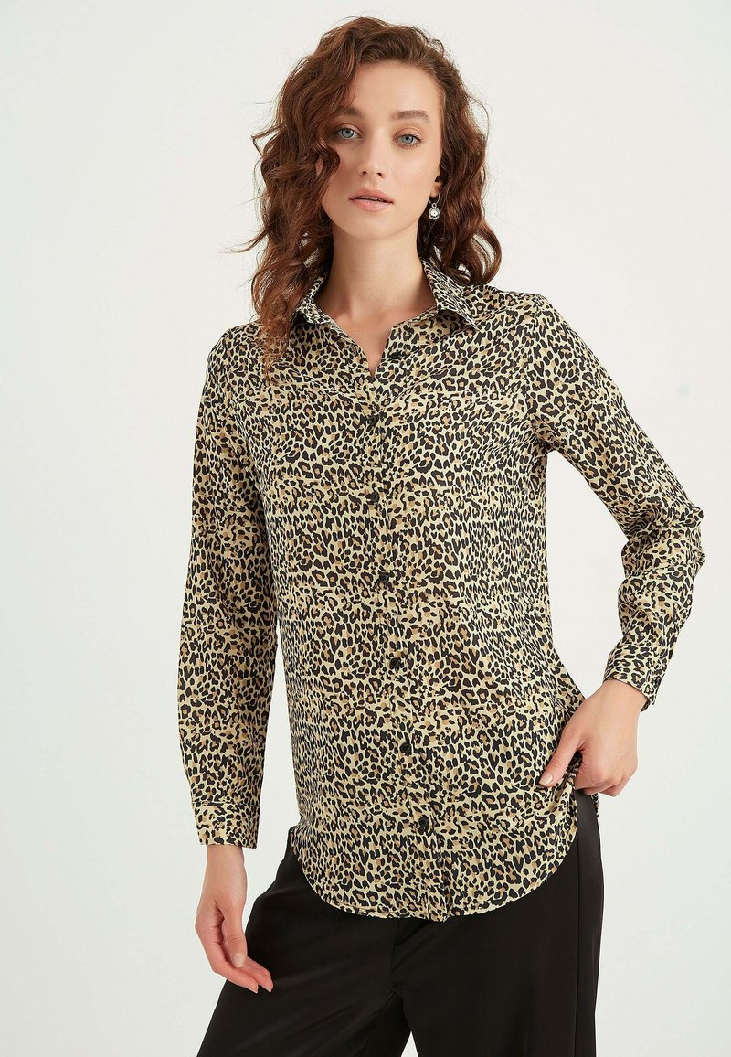 Leopard-mønstret skjorte med knapper i beige og sort, med spids krave, lange ærmer og lige kant med knapdetaljer.