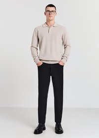 Beige Strick-Polo-Pullover mit Kragen und drei Knöpfen, kombiniert mit schwarzen Slim-Fit-Hosen und schwarzen Stiefeletten. Minimalistisches Design.