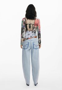 Langarmshirt mit buntem Grafikdruck und transparentem Rücken; kombiniert mit hellblauen, weit geschnittenen Jeans mit gestickten Taschen.